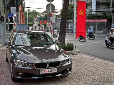 Carro de luxo importado junto a bandeiras comunistas no Vietnã - a lógica socialista